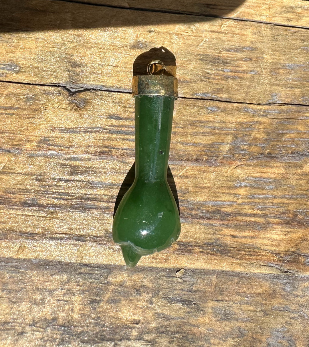 Close up of a vintage jade Figa pendant with brass cap and loop on weathered wood.