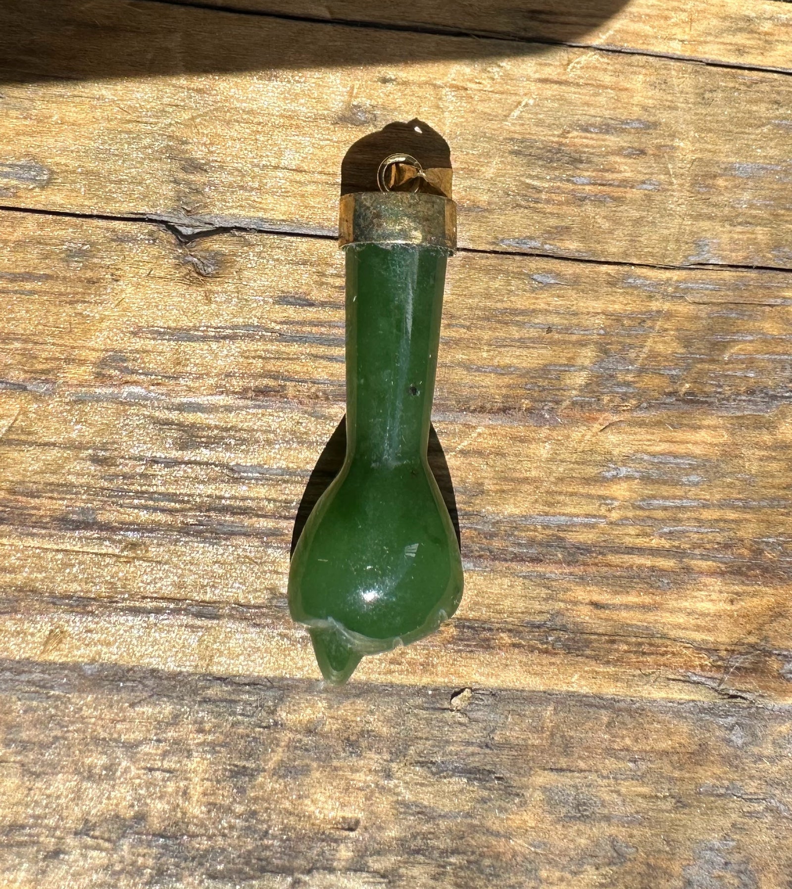 Close up of a vintage jade Figa pendant with brass cap and loop on weathered wood.