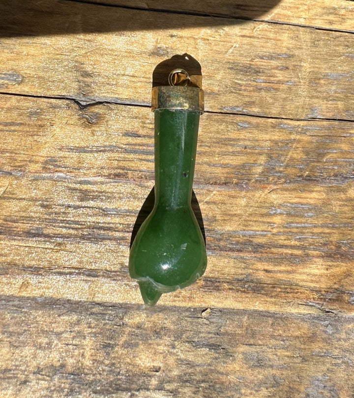 Close up of a vintage jade Figa pendant with brass cap and loop on weathered wood.