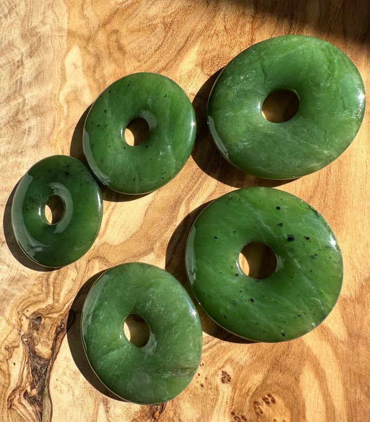 Group of five green jade donut beads arranged on a wooden surface