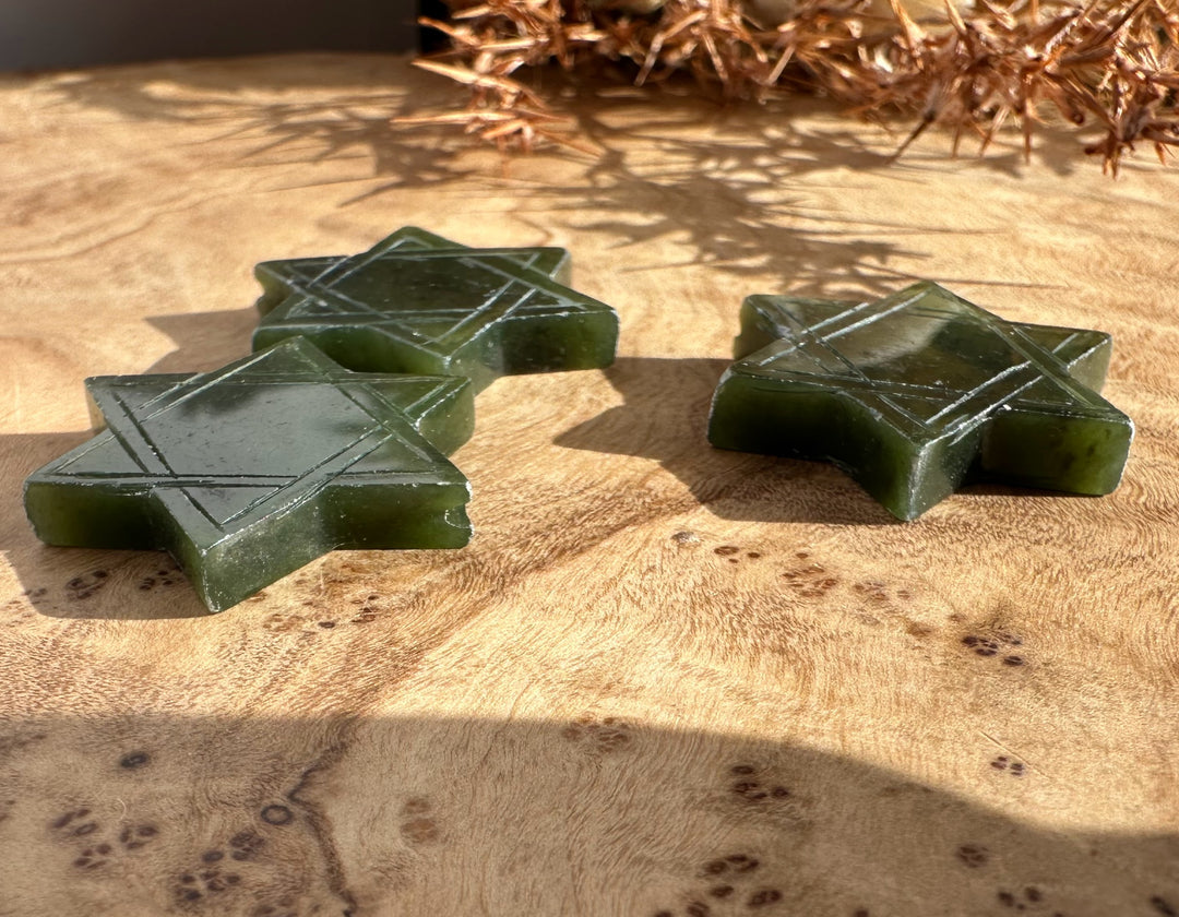 Green jade Star of David shapes with etched lines displayed on wood
