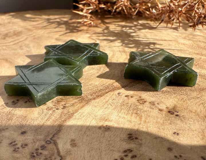 Green jade Star of David shapes with etched lines displayed on wood