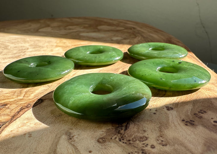 Five green jade donut beads on a sunlit wood table