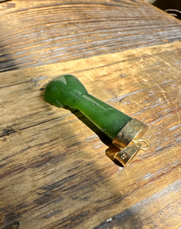 Vintage green jade figa pendant with a gold-tone cap and hanging loop on a rustic wooden surface.