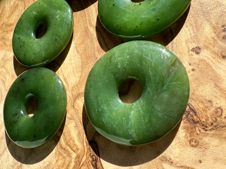 Green Canadian Jade donut pendants with central holes arranged on a wooden surface