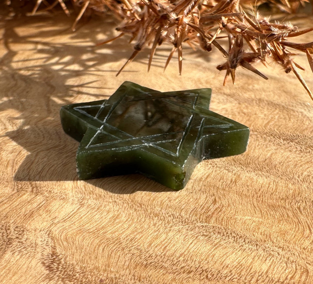 Dark green jade Star of David with etched lines lying on beige fabric