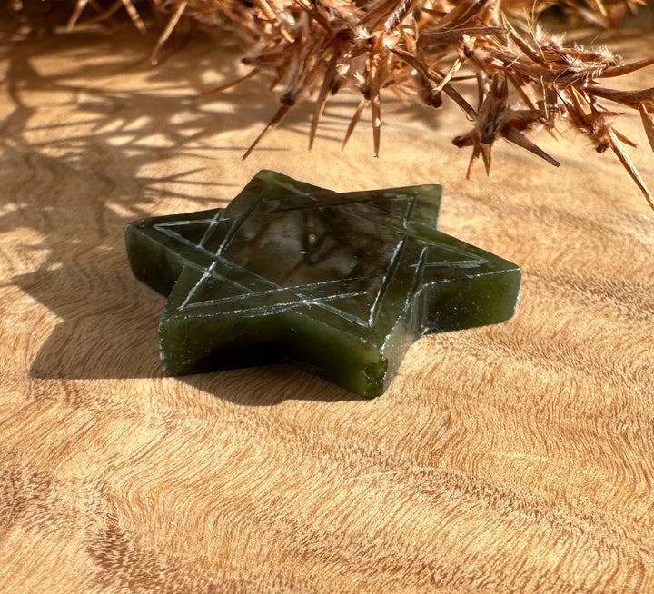 Dark green jade Star of David with etched lines lying on beige fabric