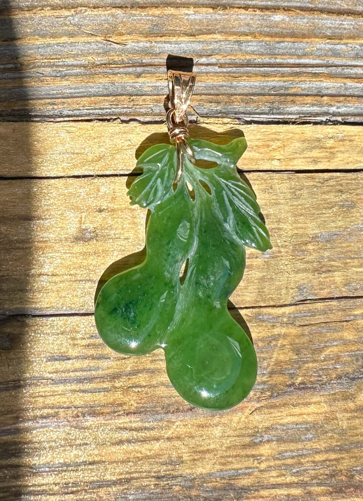 Green jade gourd pendant with leaf design hanging from a copper bail on a wooden surface