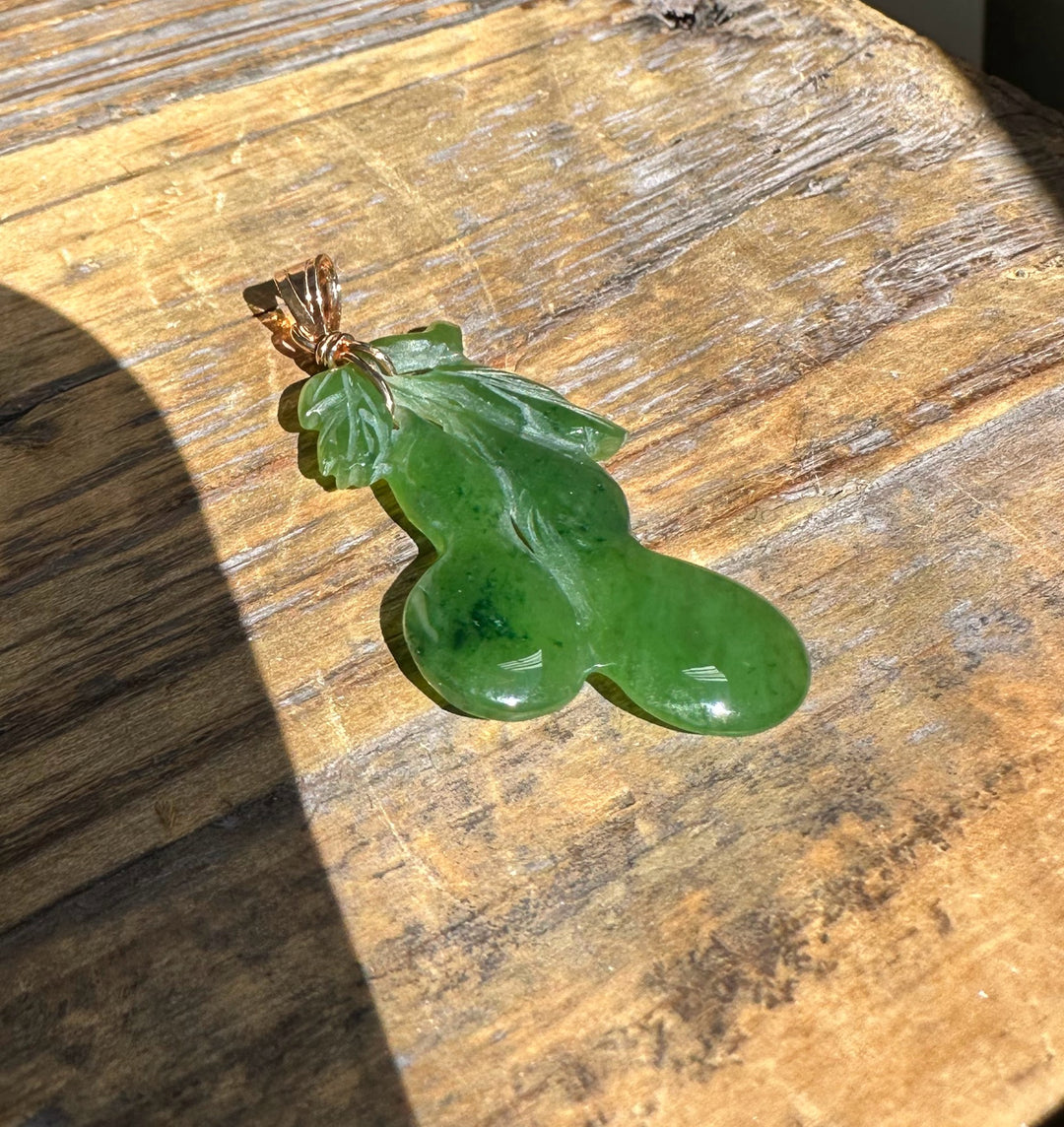 Green jade gourd pendant with carved leaf details and copper bail on a wooden surface