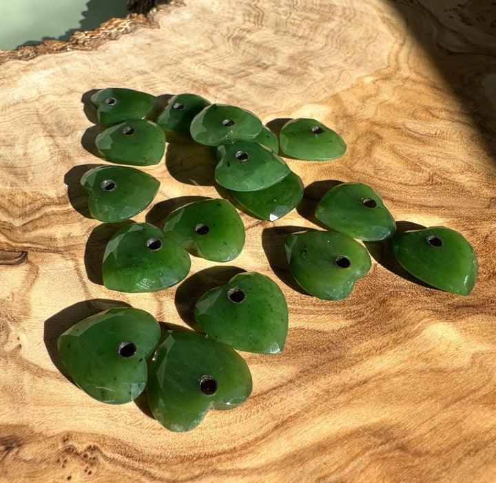 Faceted Canadian Jade heart pendants with central holes 17mm scattered on a wooden surface