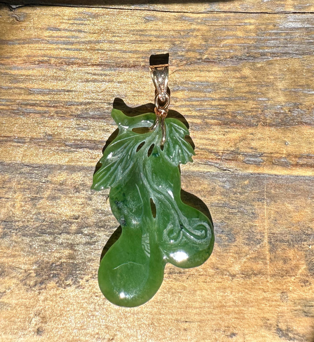 Green jade gourd pendant with flowing carved details hanging from a copper bail on a wooden surface