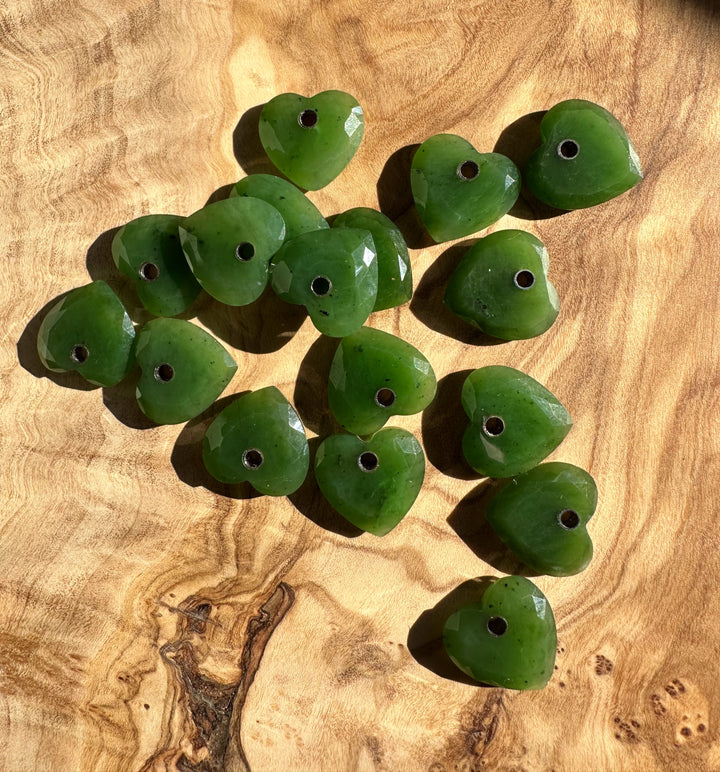 Cluster of faceted green jade heart beads with holes, arranged on a wood surface.