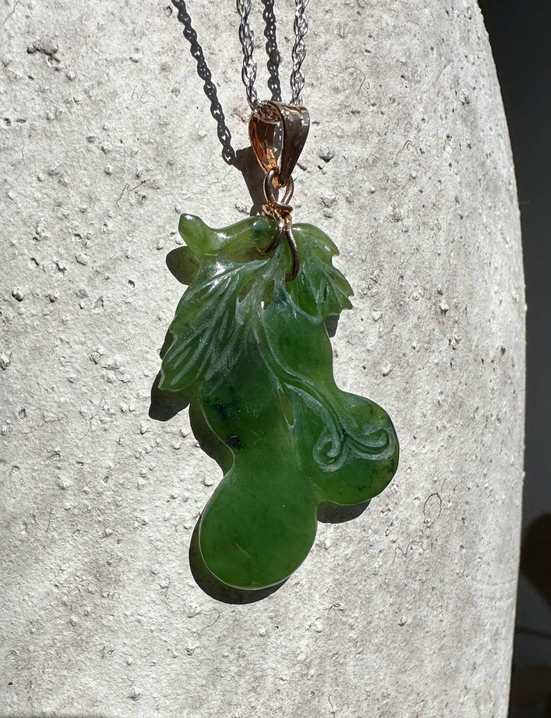 Jade gourd pendant on a chain with copper bail against a textured light stone background