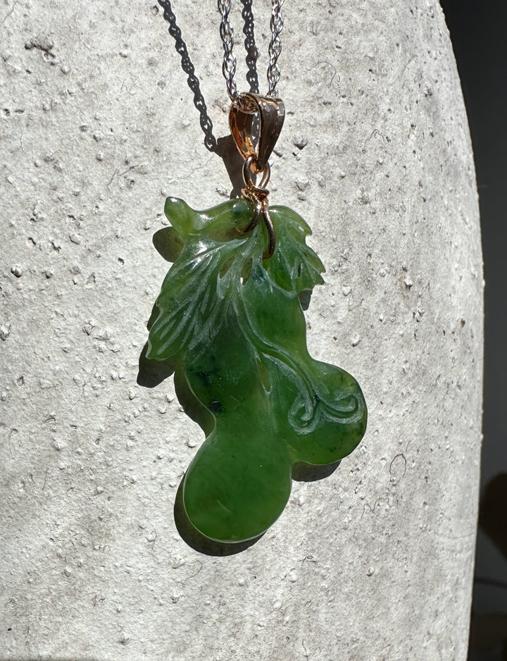 Jade gourd pendant on a chain with copper bail against a textured light stone background