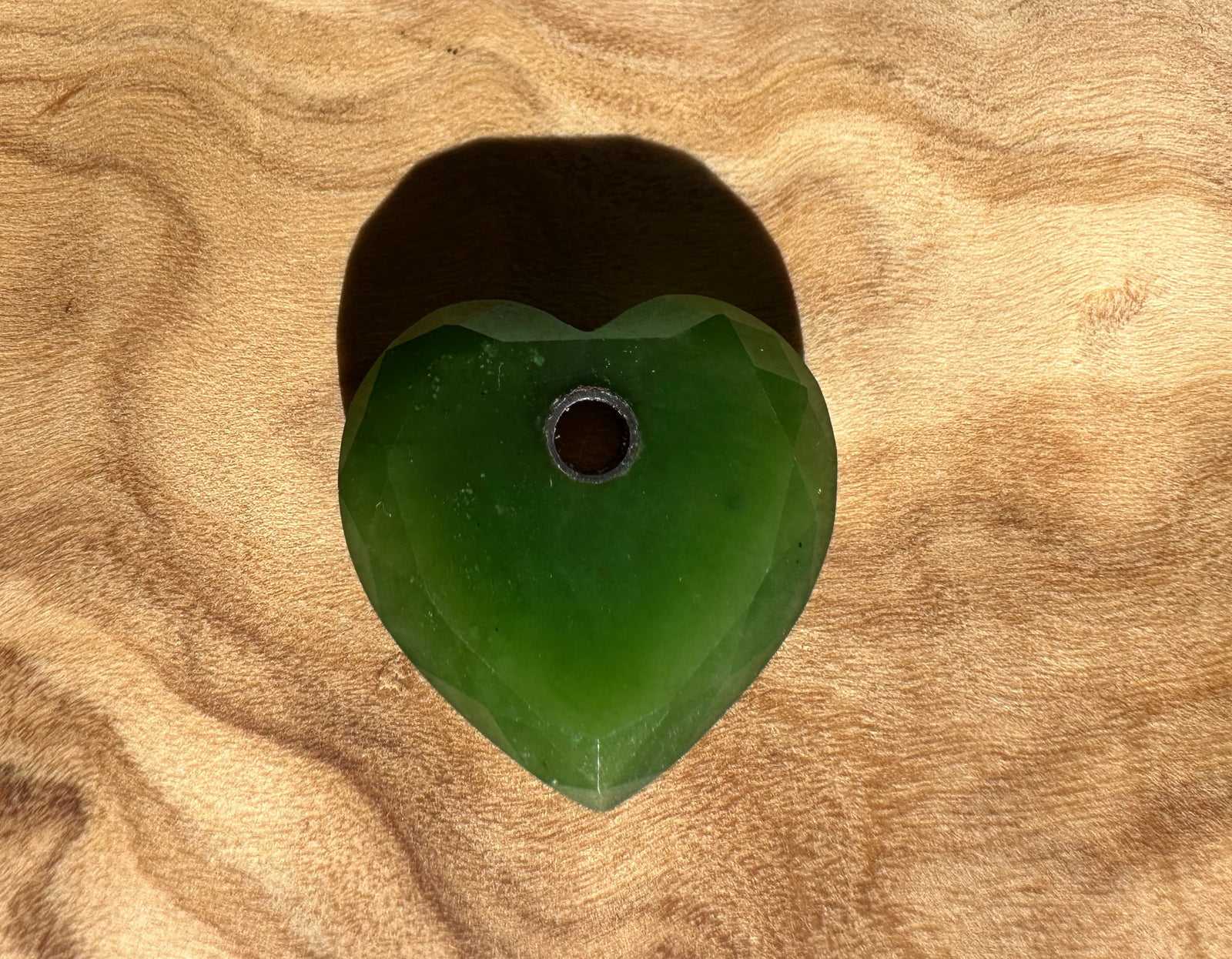 Single faceted Canadian Jade heart pendant with central hole 17mm on a wooden surface