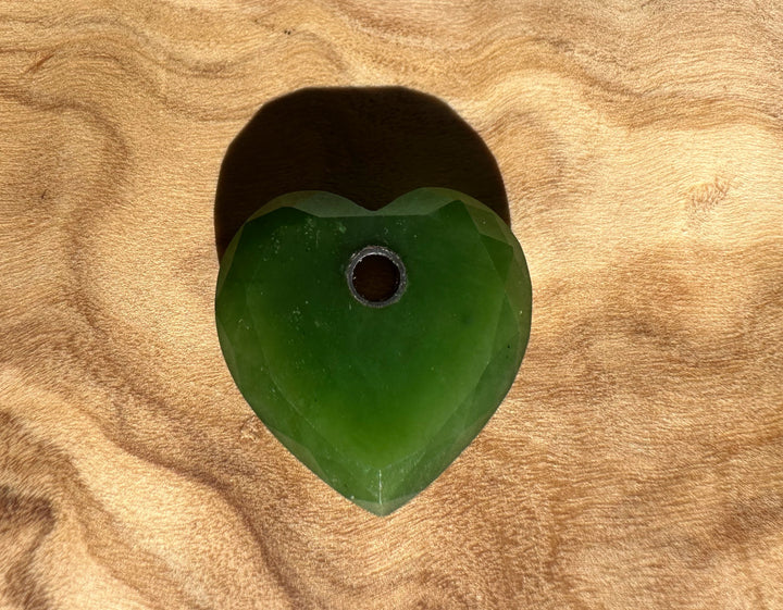 Single faceted Canadian Jade heart pendant with central hole 17mm on a wooden surface
