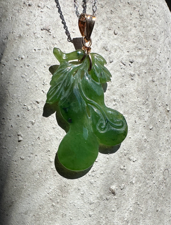 Green jade gourd pendant with carved leaf details on a silver chain against a light stone background
