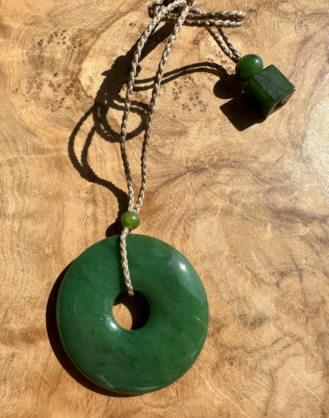 Green Jade PI Pendant on a brown cord. Resting on a wooden base