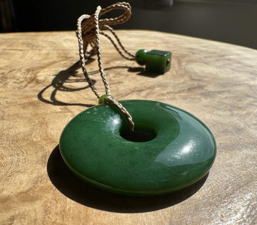 Green Jade PI Pendant on a brown cord. Resting on a wooden base