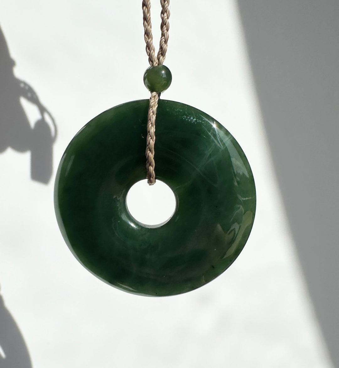Dark Green Jade against a white background, on a brown cord