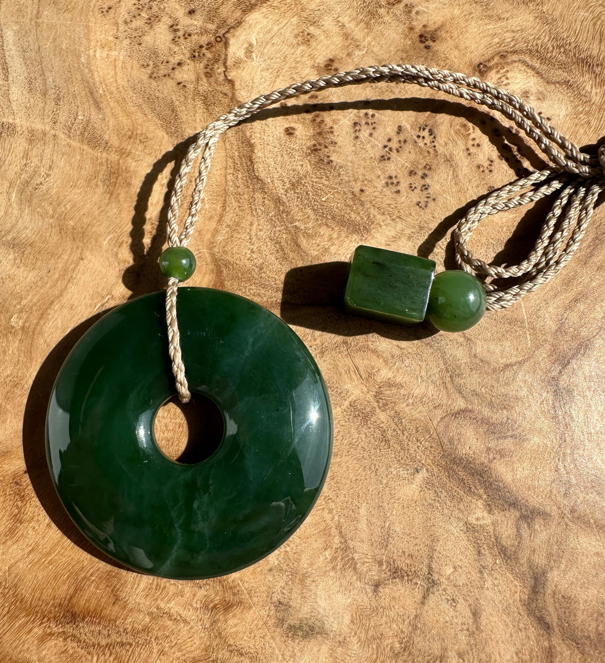 Green Jade PI Pendant on a brown cord. Resting on a wooden base