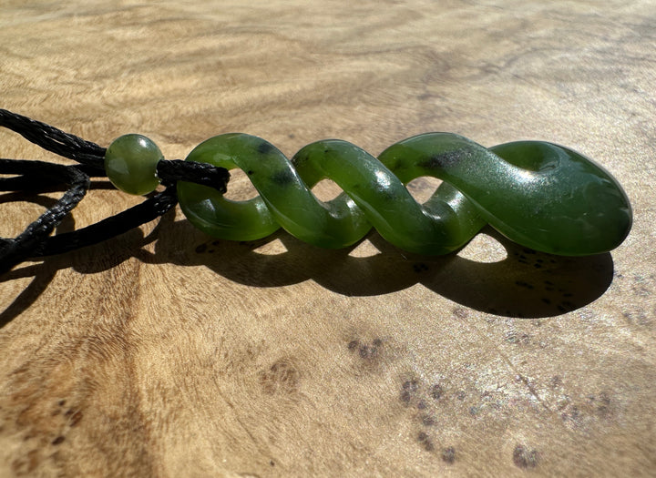 Green jade twist pendant on a black cord, laying on top of a wooden surface