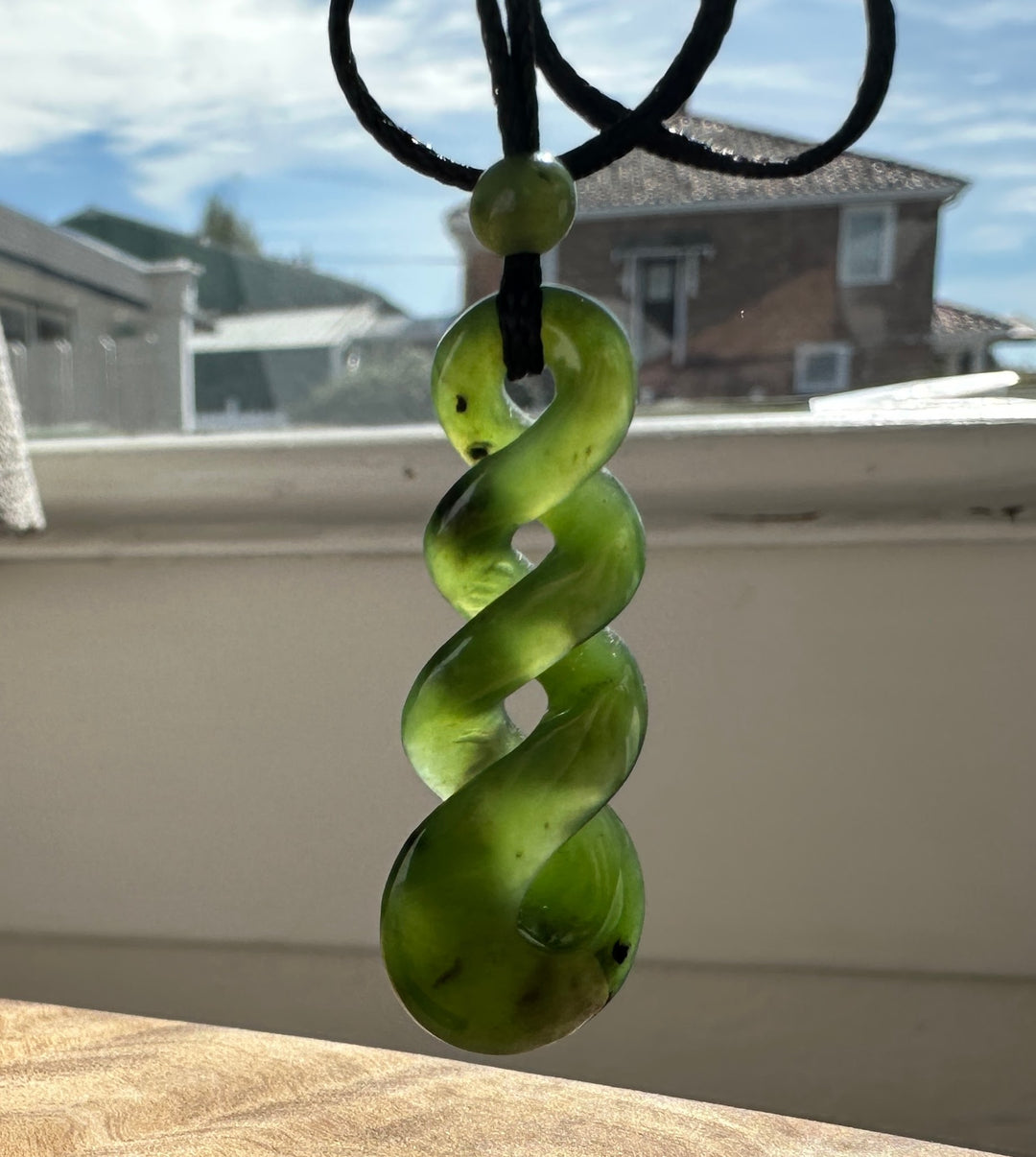Green jade twist pendant on a black cord, in front of a sunny window