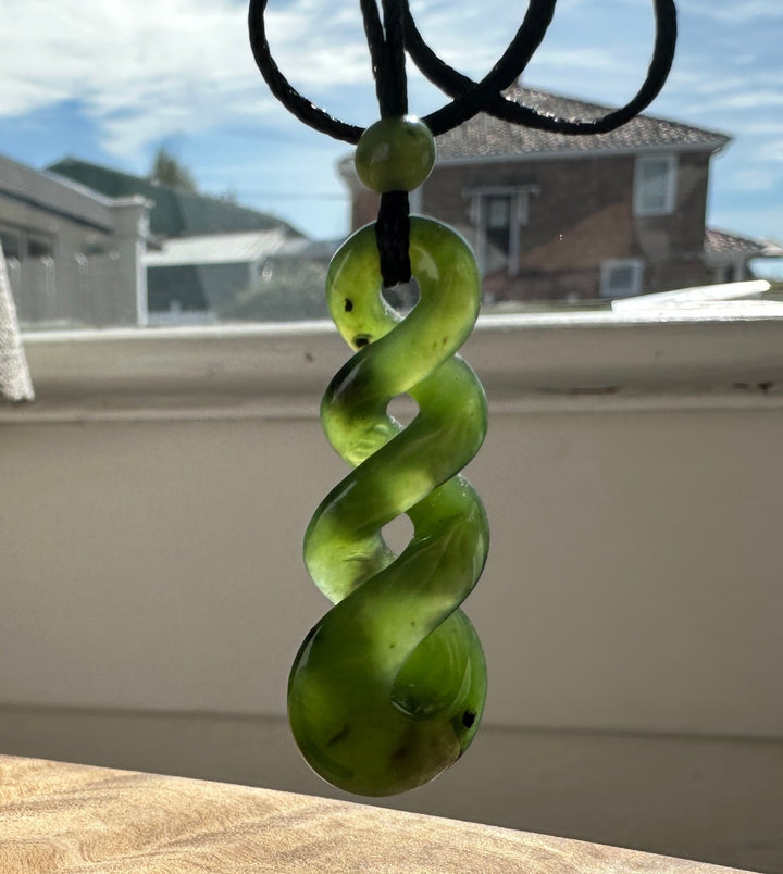 Green jade twist pendant on a black cord, in front of a sunny window