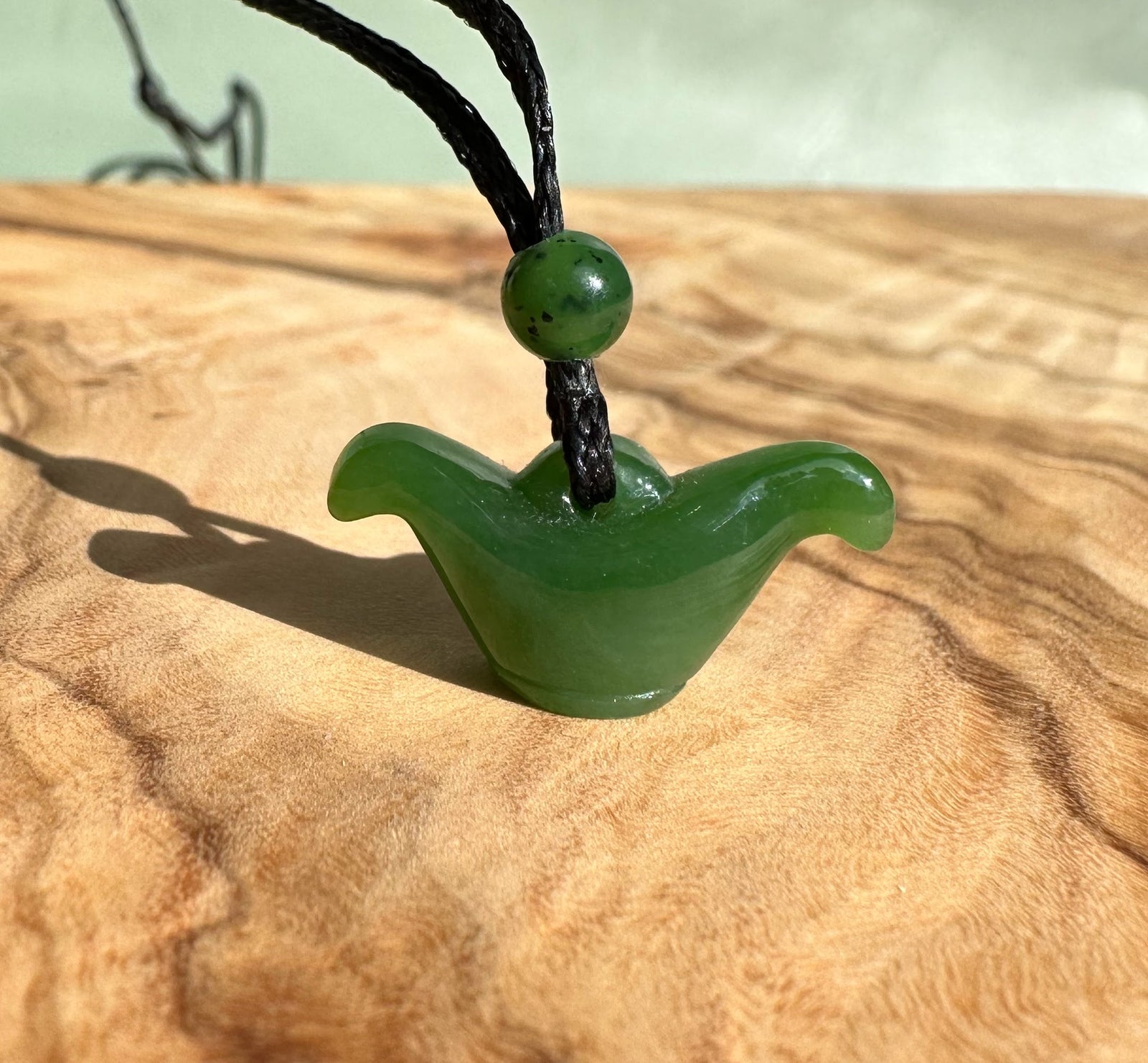 Green nephrite jade pendant with a curved winged shape on a black cord and round bead