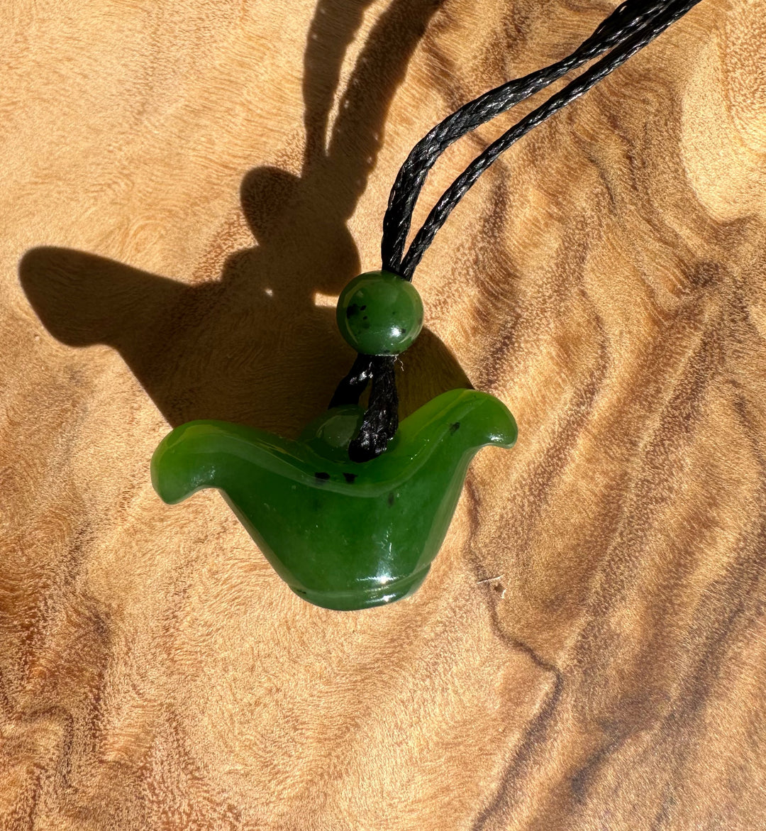 Green nephrite jade pendant on black cord resting on wood with sunlight highlighting its glossy curved form