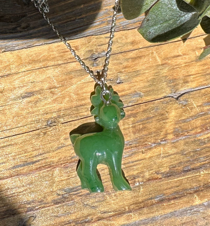 Green nephrite jade deer pendant on a silver chain resting on a wooden surface in bright light
