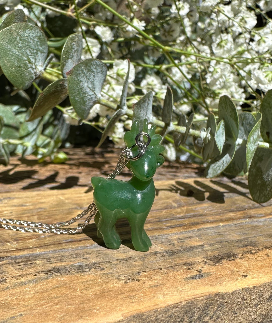 Close-up of green nephrite jade deer pendant on a silver chain against a wooden background