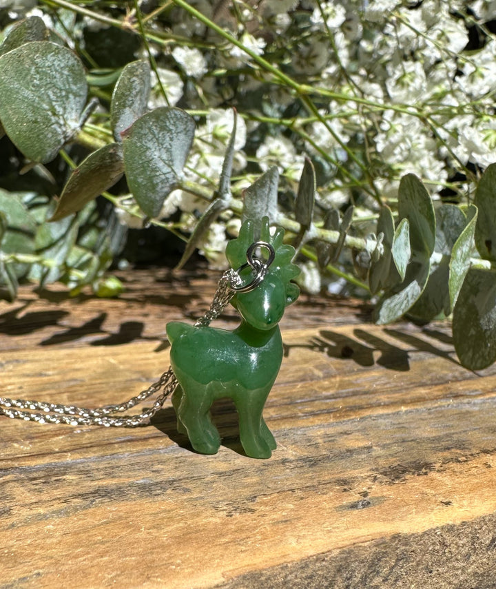 Close-up of green nephrite jade deer pendant on a silver chain against a wooden background