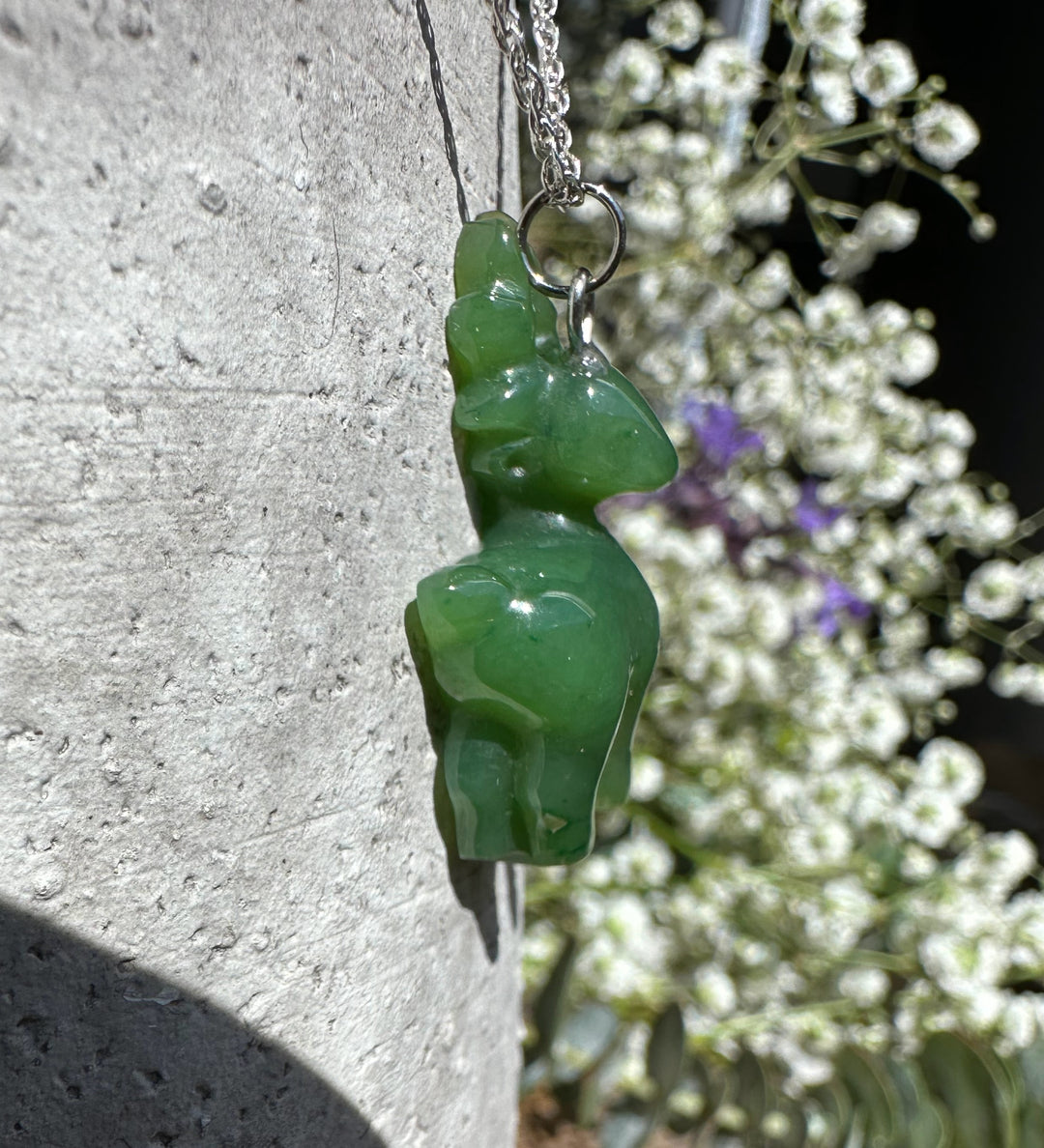 Close-up of green nephrite jade deer pendant on a silver chain with a metal ring bail