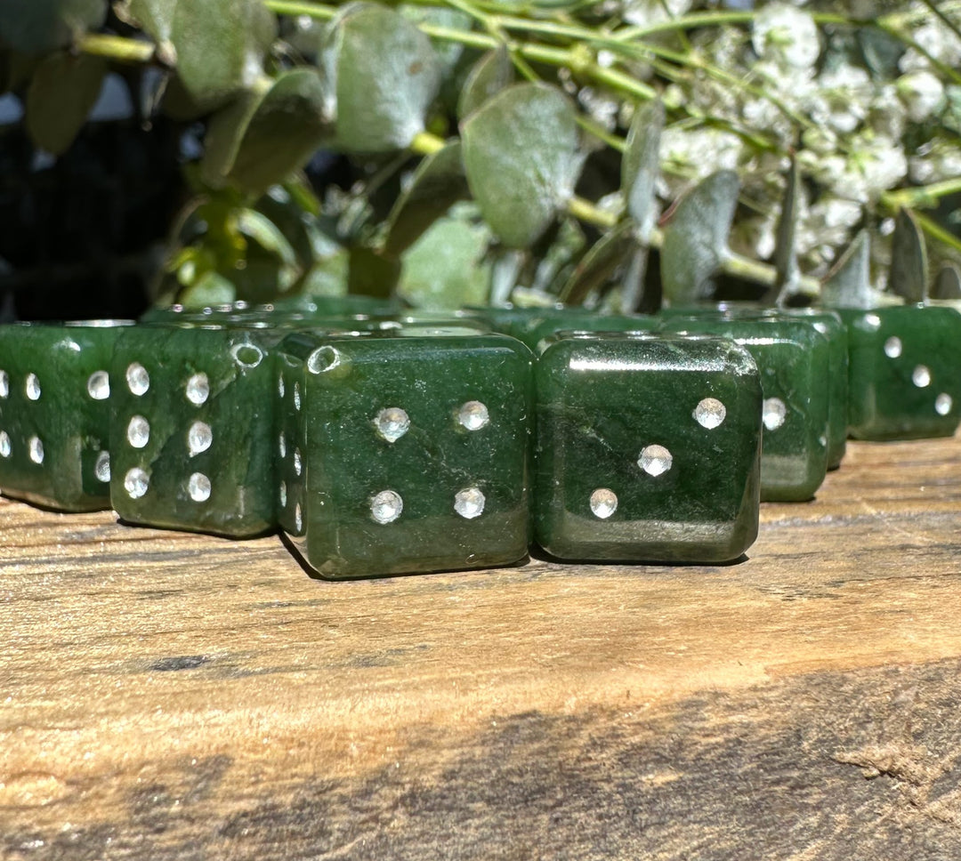 Close up of green jade dice with white pips on a weathered wooden surface.