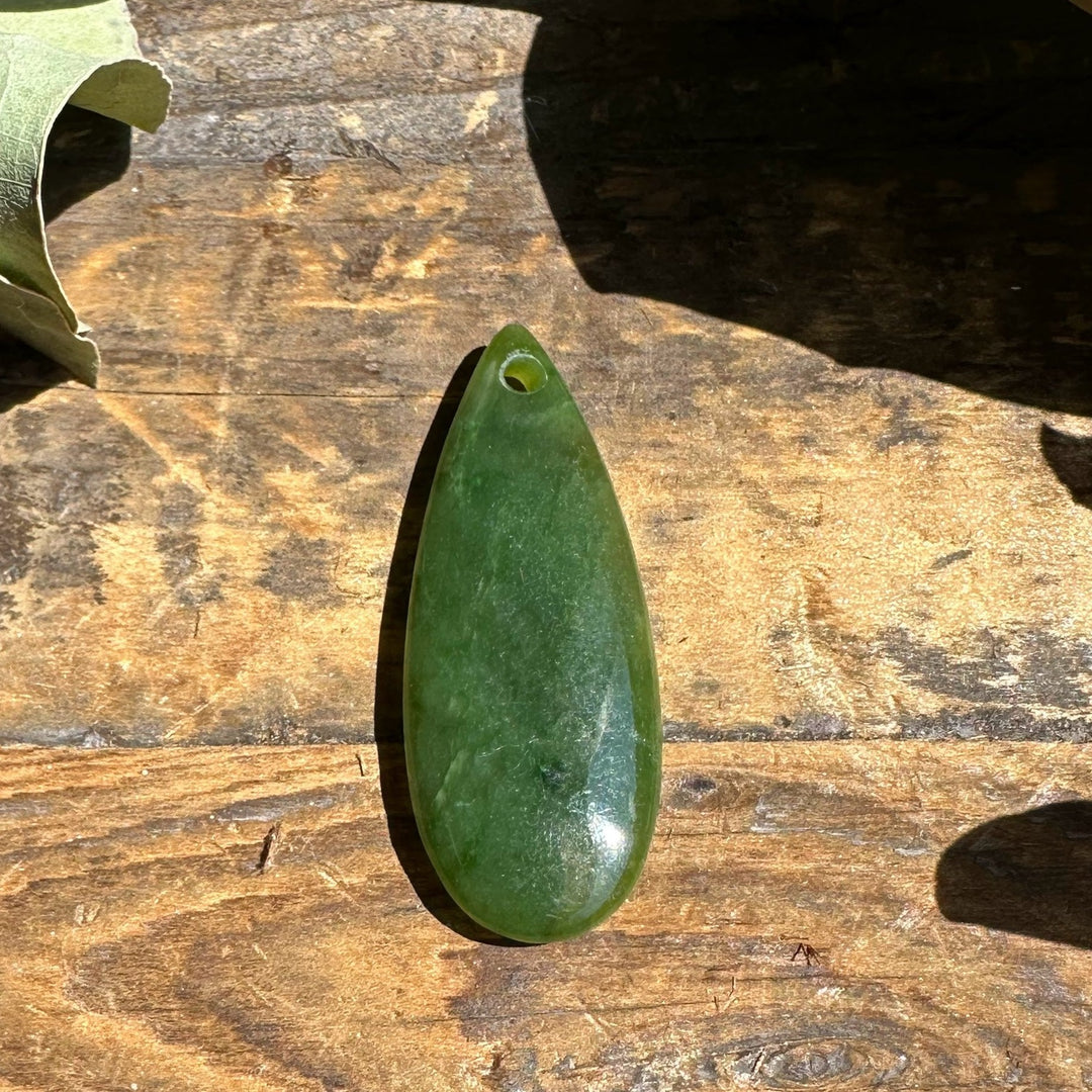 Green teardrop shaped Canadian jade pendant with a small hole at the top for a cord