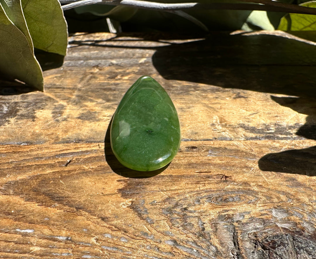 Canadian Jade teardrop gemstone 1.7 inches on weathered wood surface