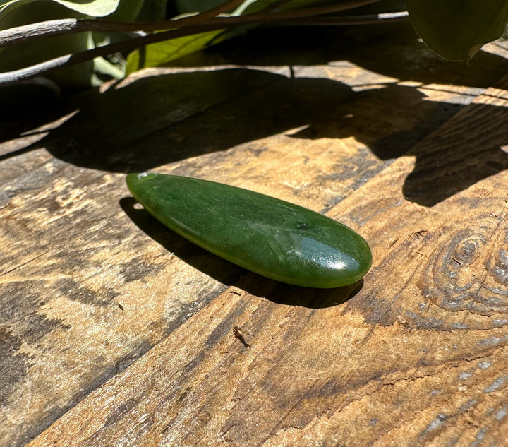 Canadian Jade Teardrop pendant polished green jade with a top hole resting on a sunlit wooden surface