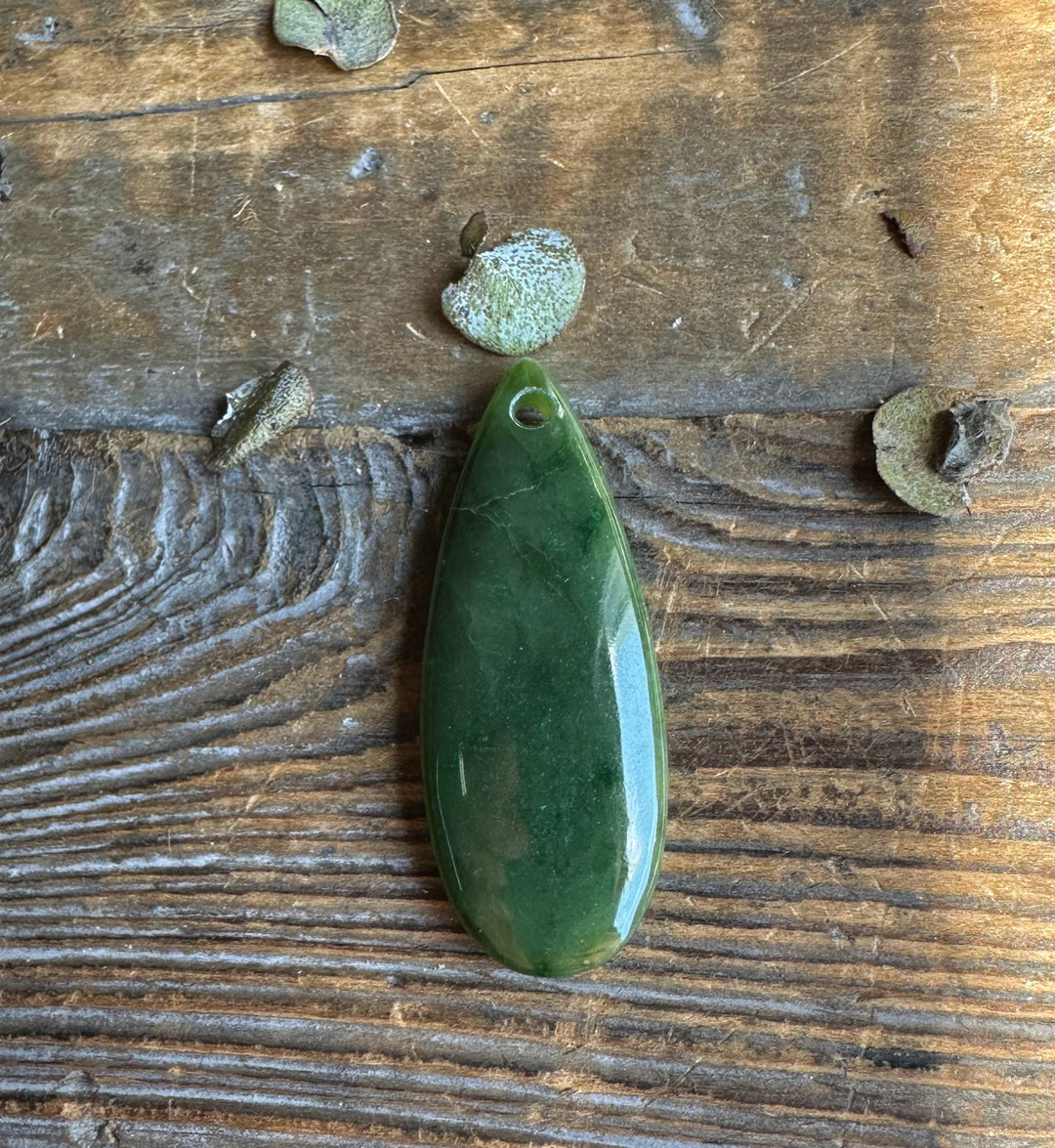 Polished green Canadian Jade Teardrop pendant with a top hole resting on aged wood background