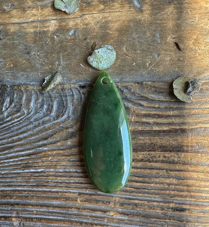 Polished green Canadian Jade Teardrop pendant with a top hole resting on aged wood background
