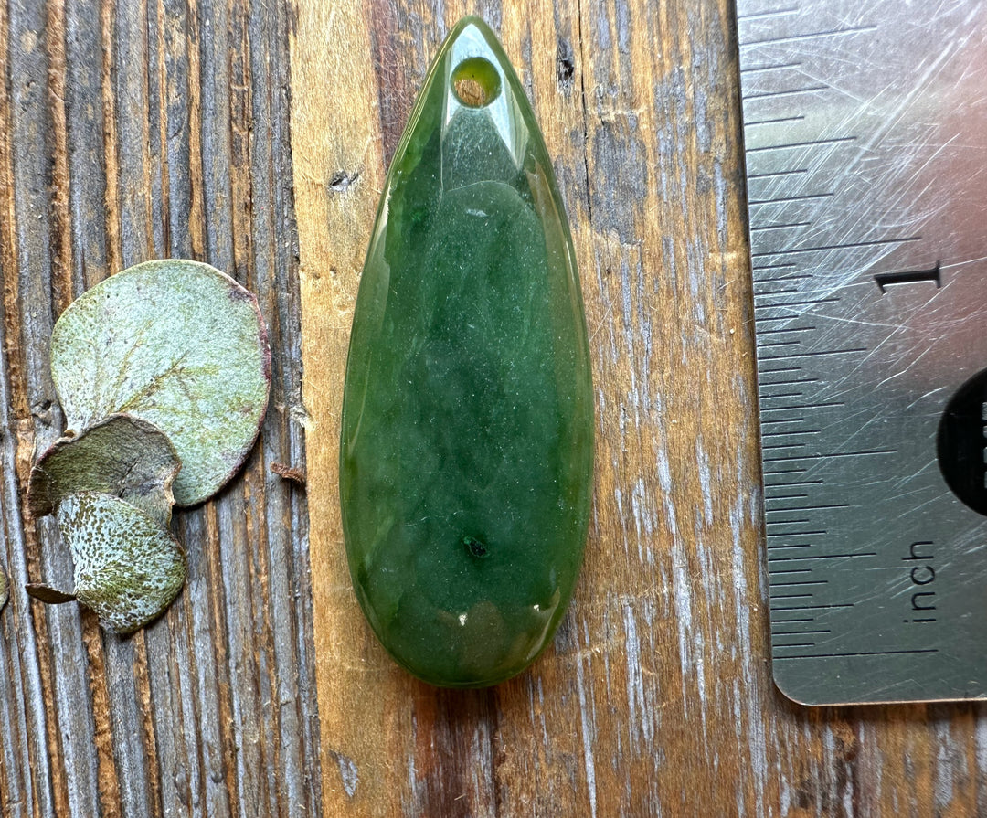 Canadian Jade Teardrop pendant 1.7 inches long with a drilled hole for cord on a wooden surface
