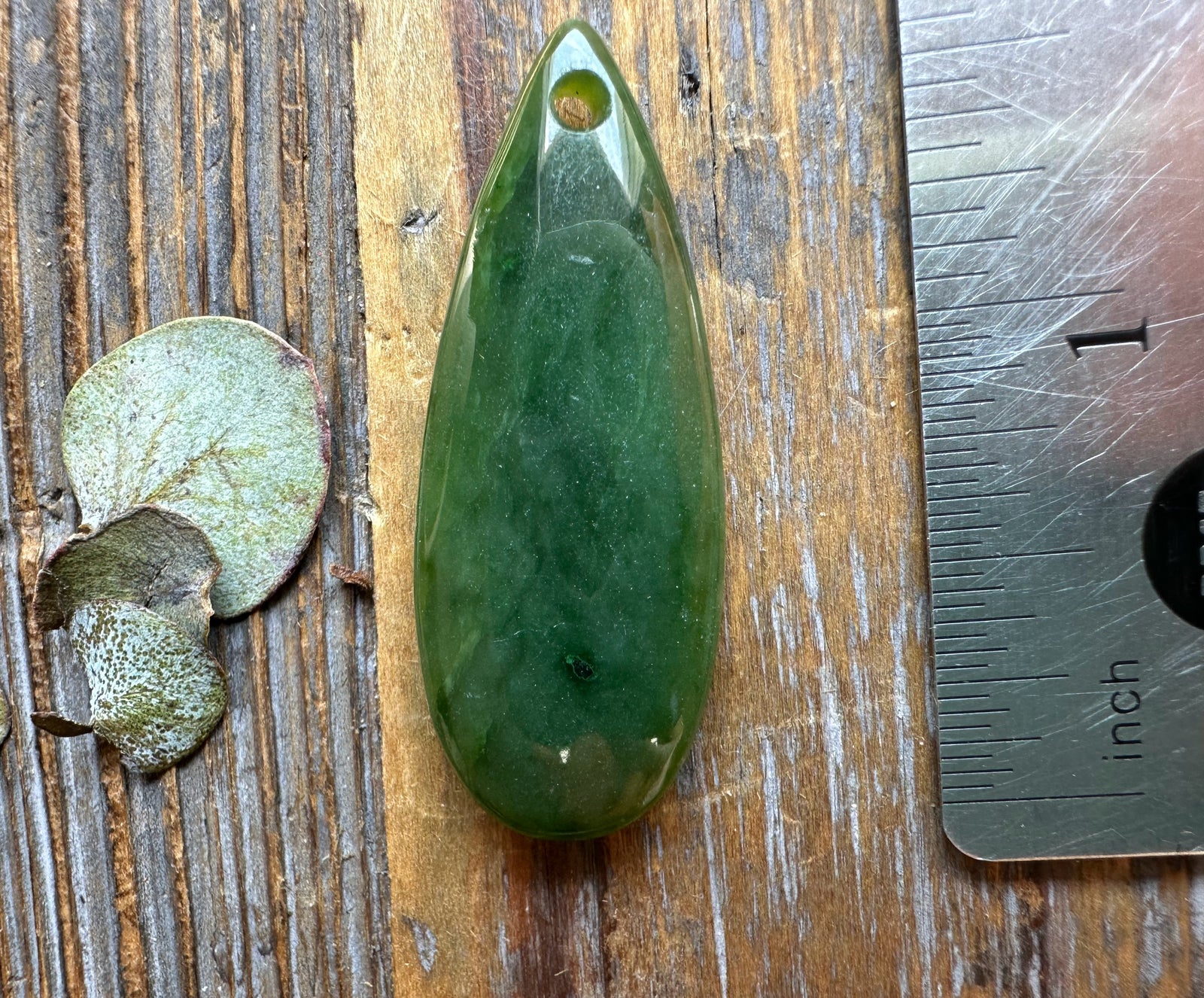 Canadian Jade Teardrop pendant 1.7 inches long with a drilled hole for cord on a wooden surface