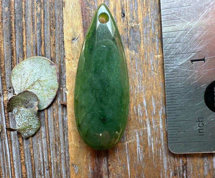 Canadian Jade Teardrop pendant 1.7 inches long with a drilled hole for cord on a wooden surface