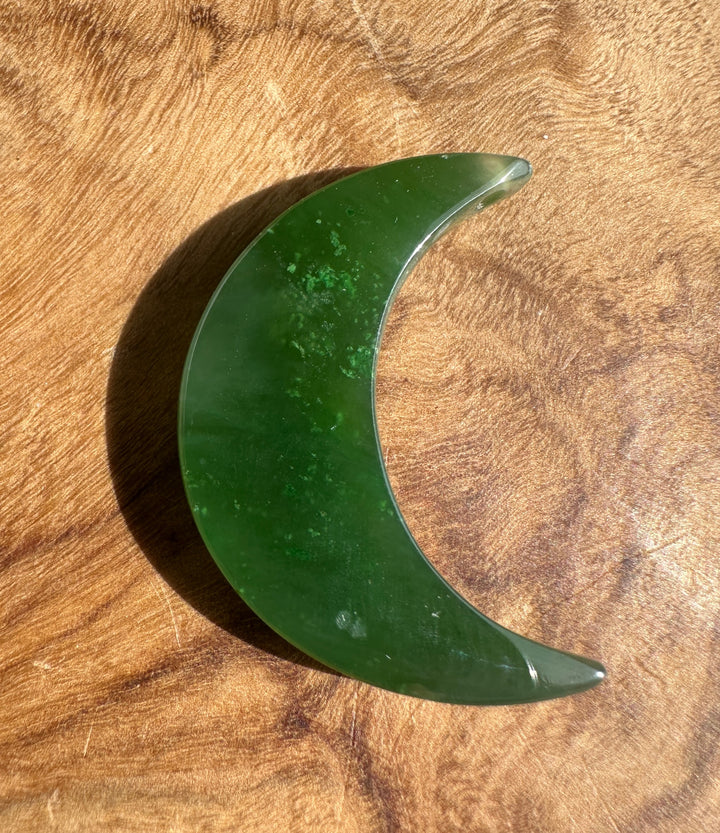 A crescent moon-shaped green jade with a polished finish, resting on a textured wooden surface.