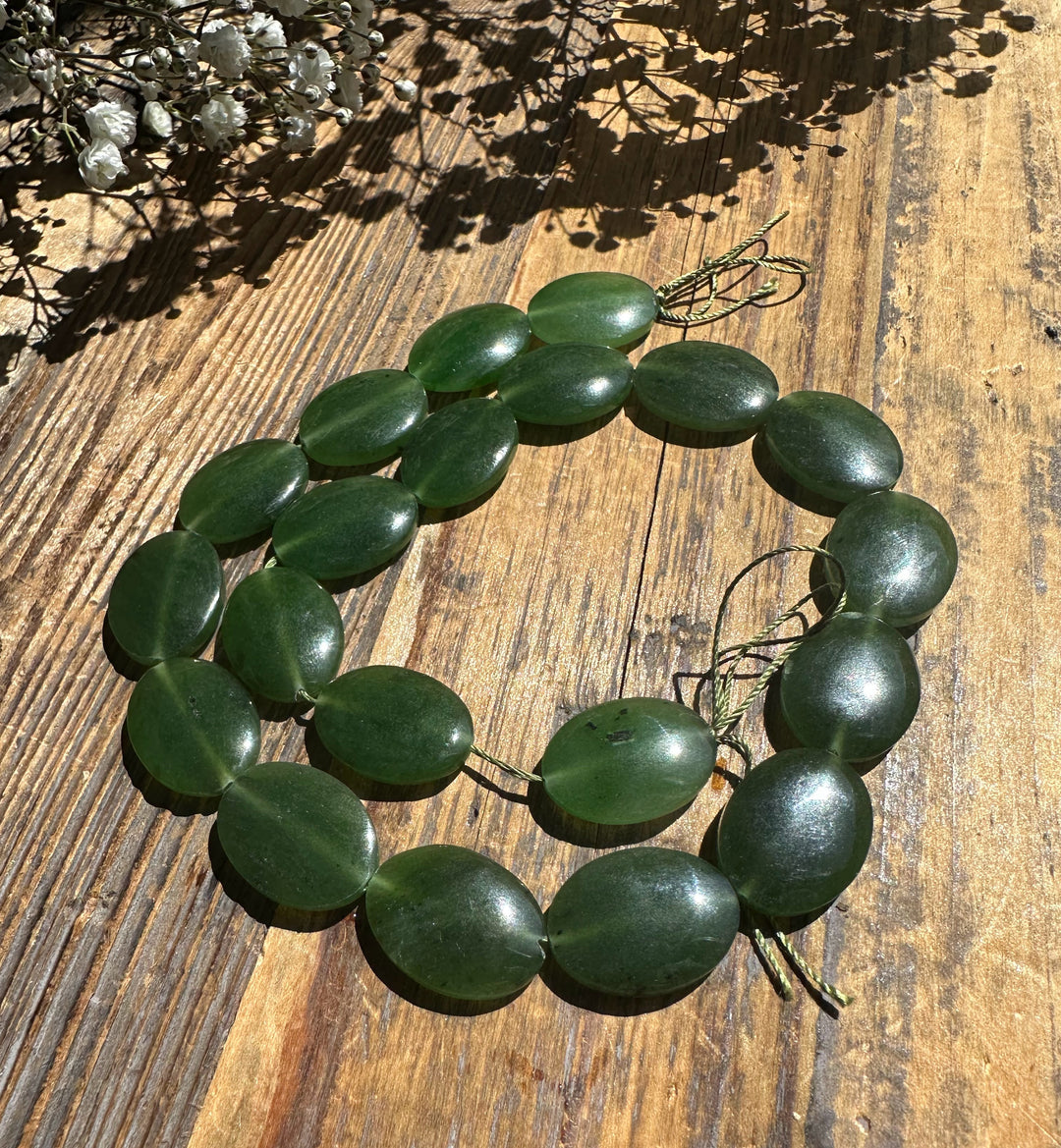 Long necklace of glossy green jade discs 20x15mm threaded on cord on a wooden surface.