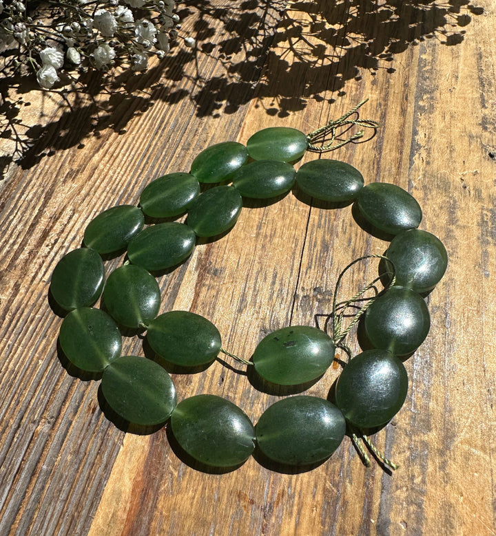 Long necklace of glossy green jade discs 20x15mm threaded on cord on a wooden surface.