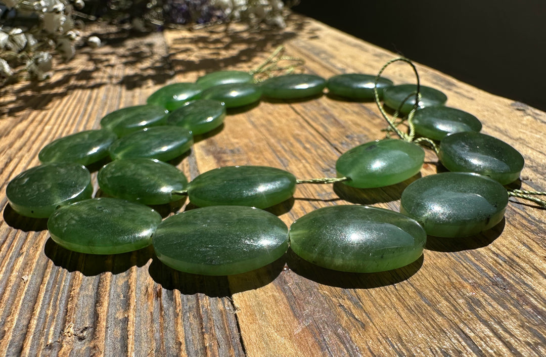 Green jade beads 20x15mm arranged as a strand on a rustic wooden surface
