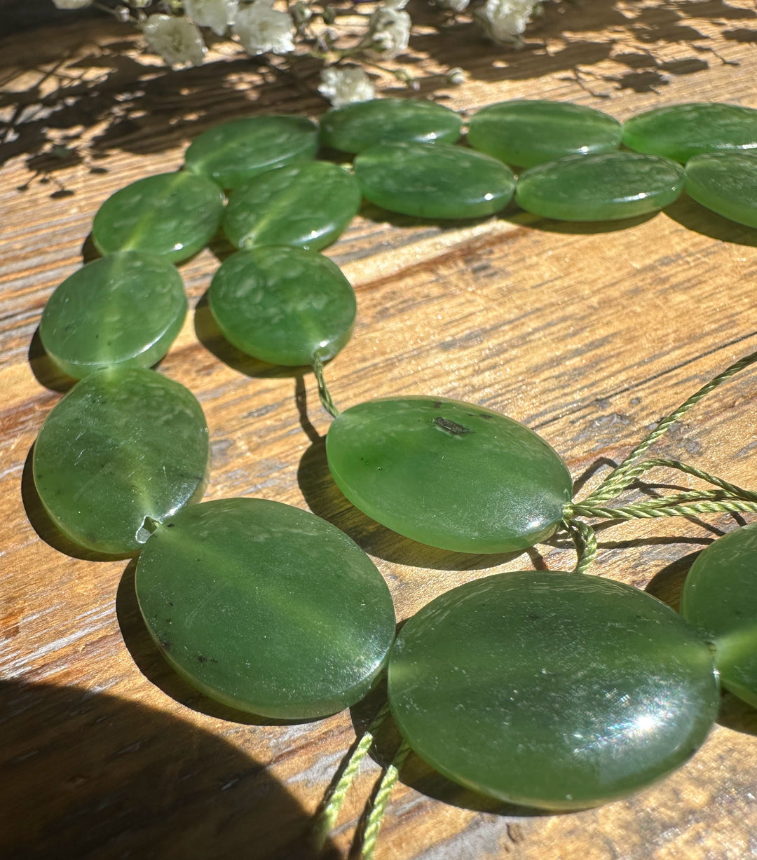 Green Canadian Jade beads 20x15mm arranged in a circular strand on a wooden surface.