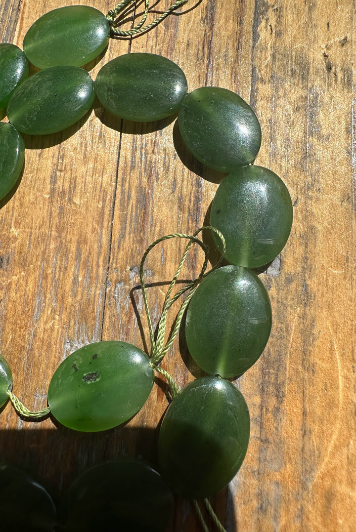 Oval green jade beads threaded on twisted cord laid on a wooden surface