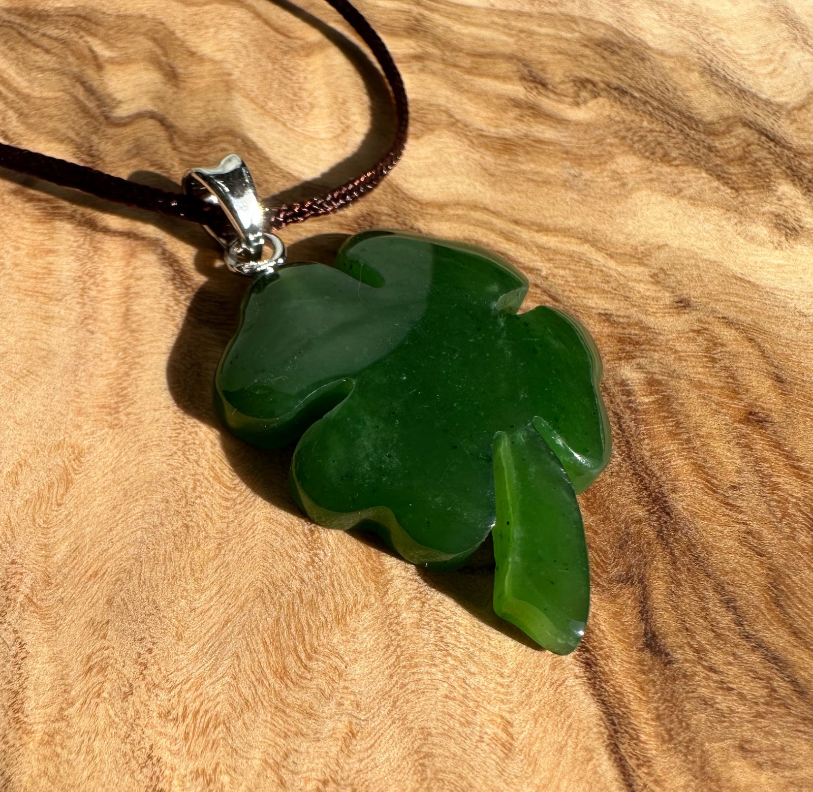 Green jade shamrock pendant with silver bail resting on a wood surface